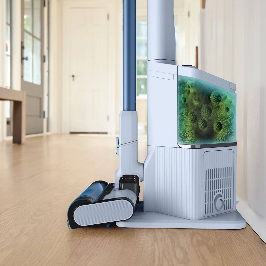 Shark handstick vacuum on its charging base with a visible dustbin in a hallway
