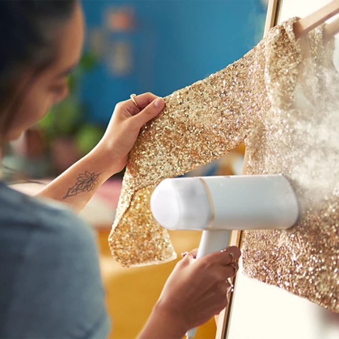 Woman steaming a gold sequined garment with a handheld garment steamer