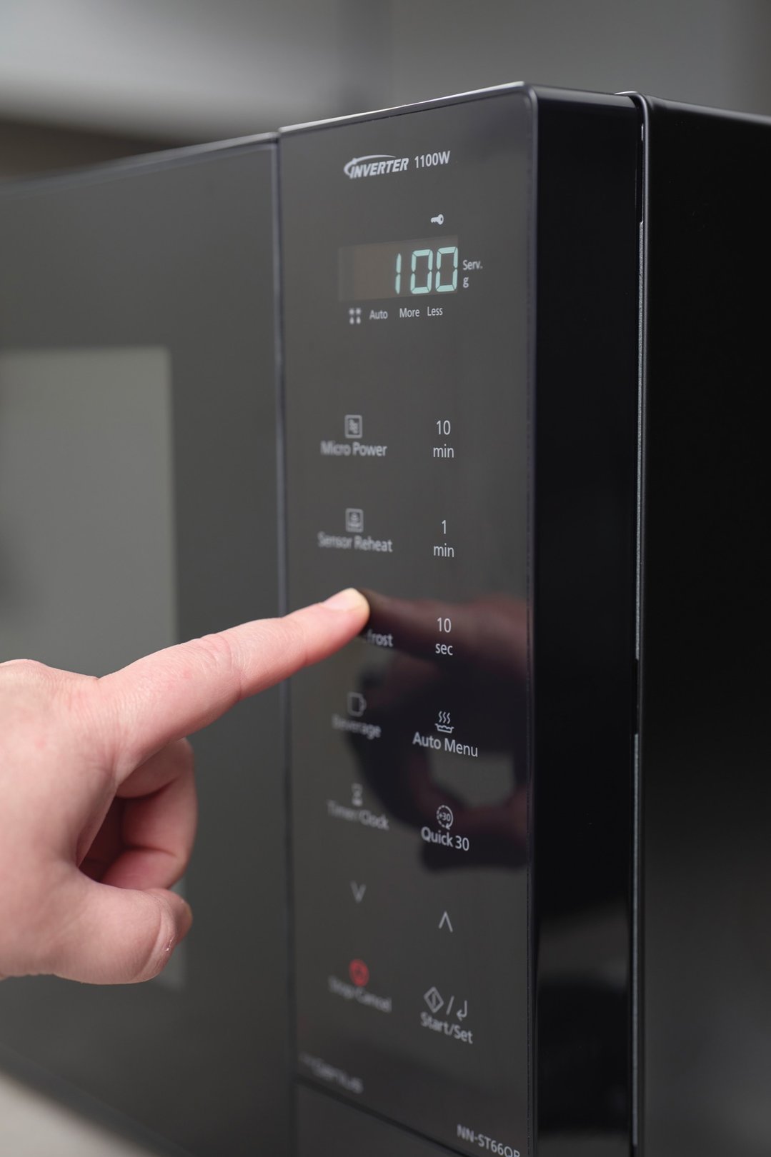 Finger pressing the 'Frost' button on a black Panasonic microwave control panel