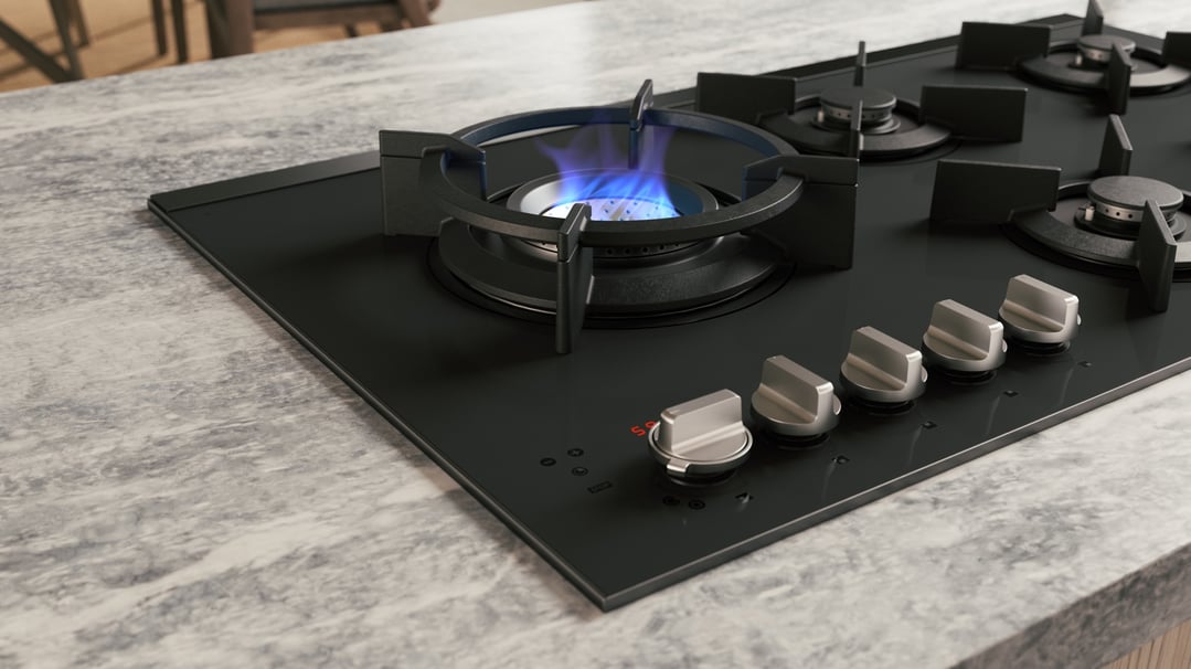 Close up of a black gas cooktop with one burner lit on a marble countertop