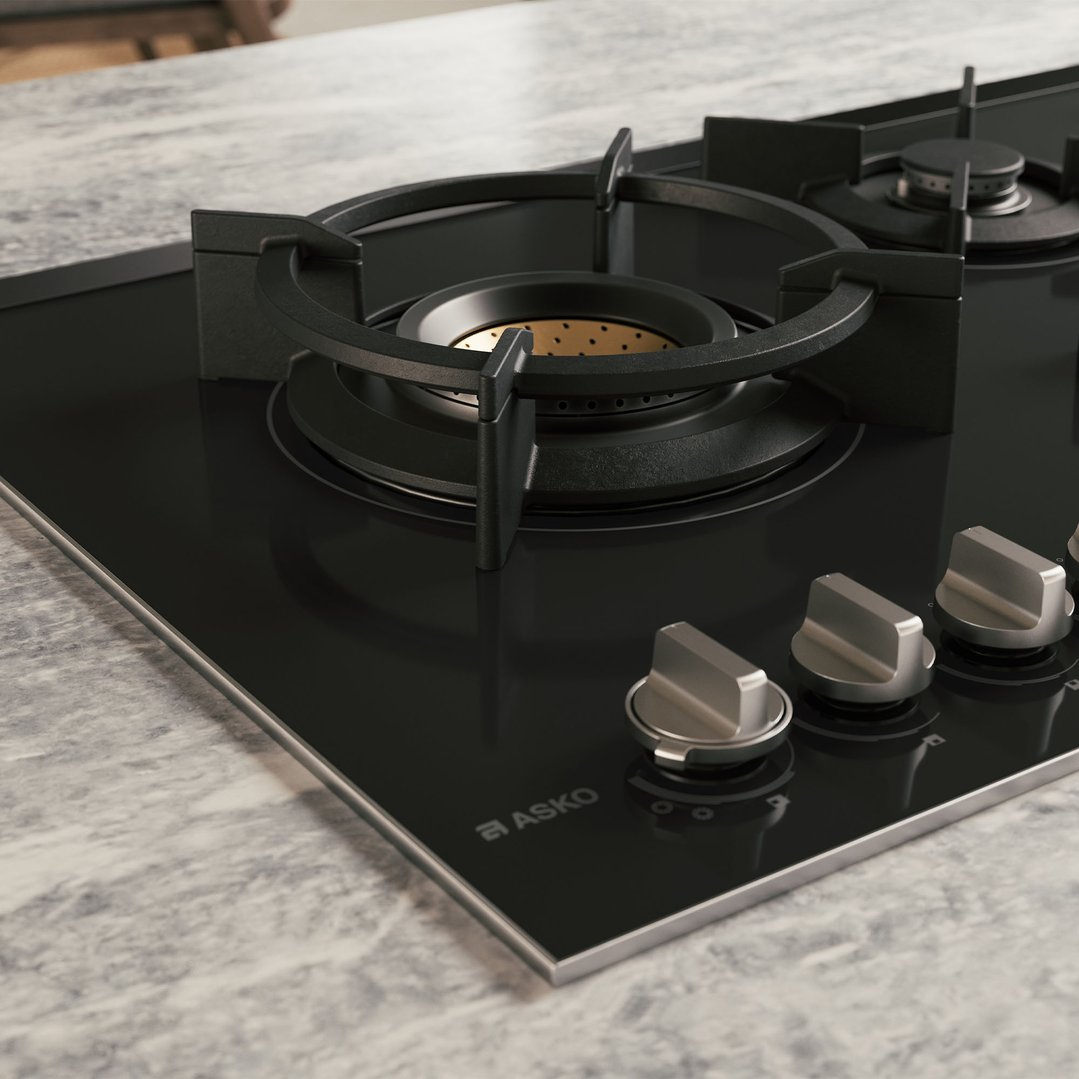 Close up of a black glass cooktop with five burners on a marble countertop