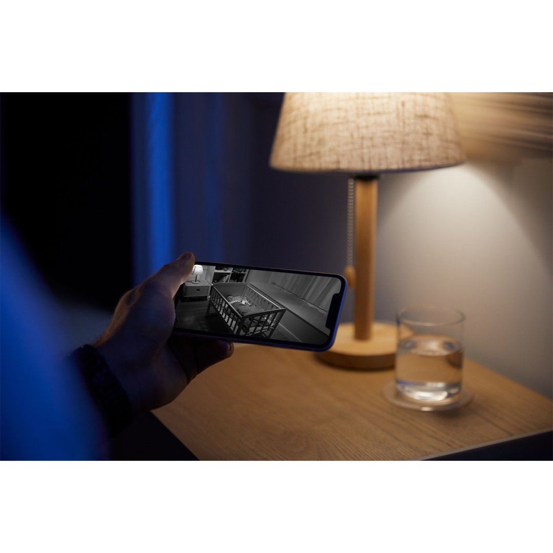 Hand holding phone displaying a baby monitor feed of a baby in a crib