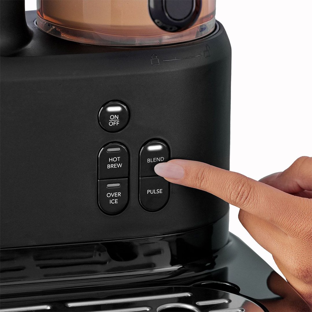 A person's hand pressing the blend button on a black coffee machine