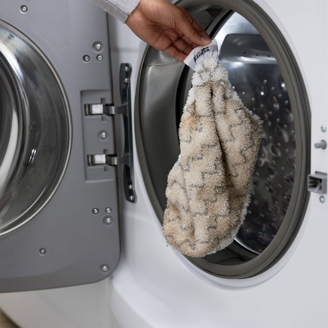 Hand holding a steam mop pad over an open washing machine