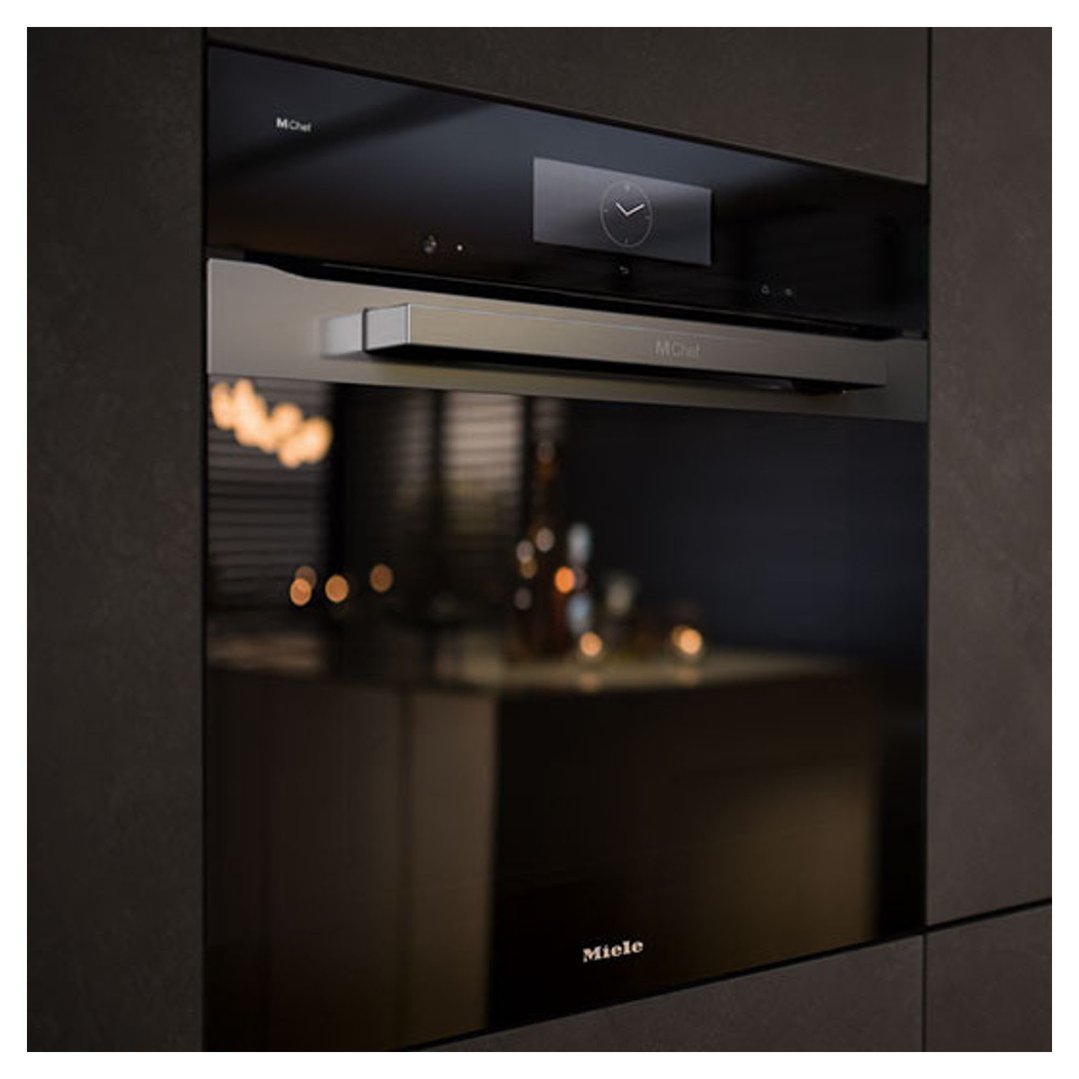 A built-in Miele oven with a dark glass door and a silver handle in a kitchen