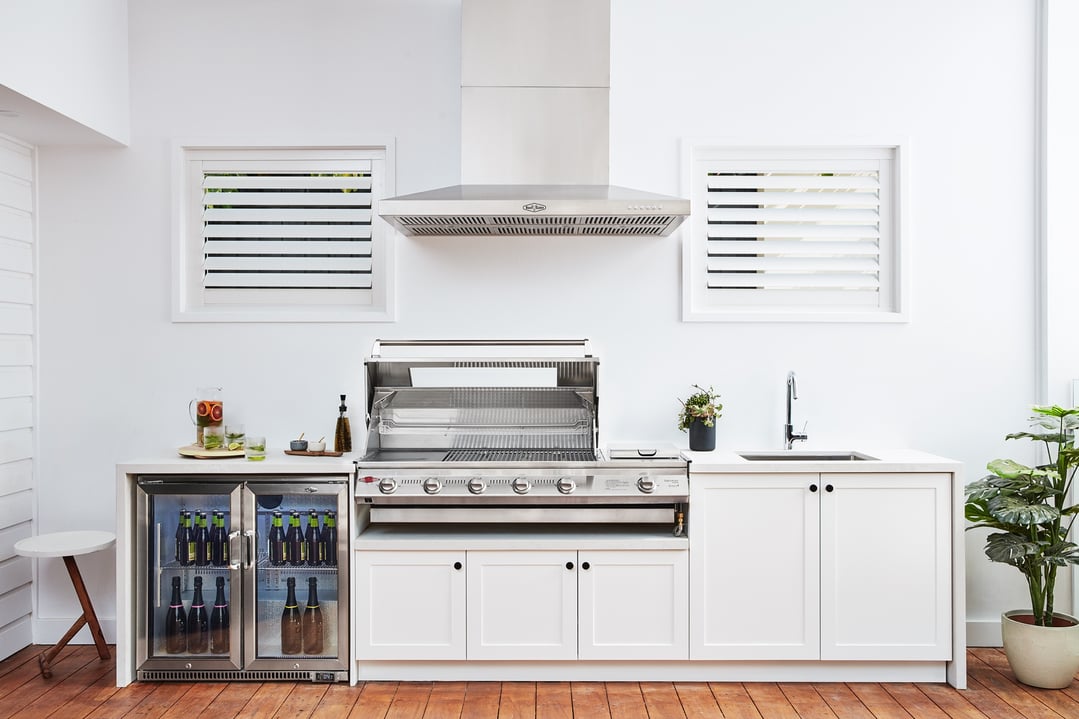 Outdoor kitchen with a rangehood, grill, sink, and beverage fridges