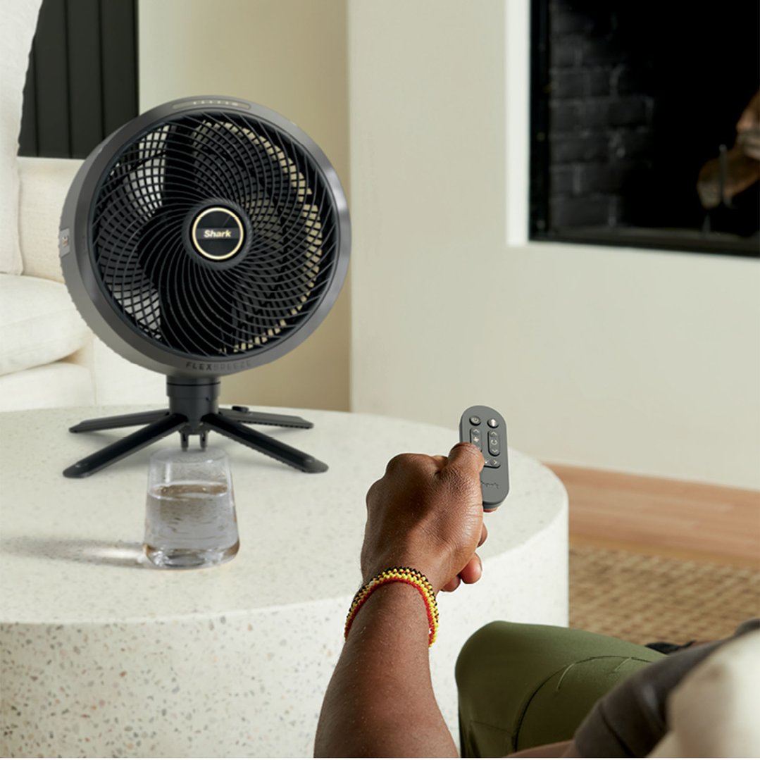 Person holding a remote control, with a Shark FlexBreeze fan on a table