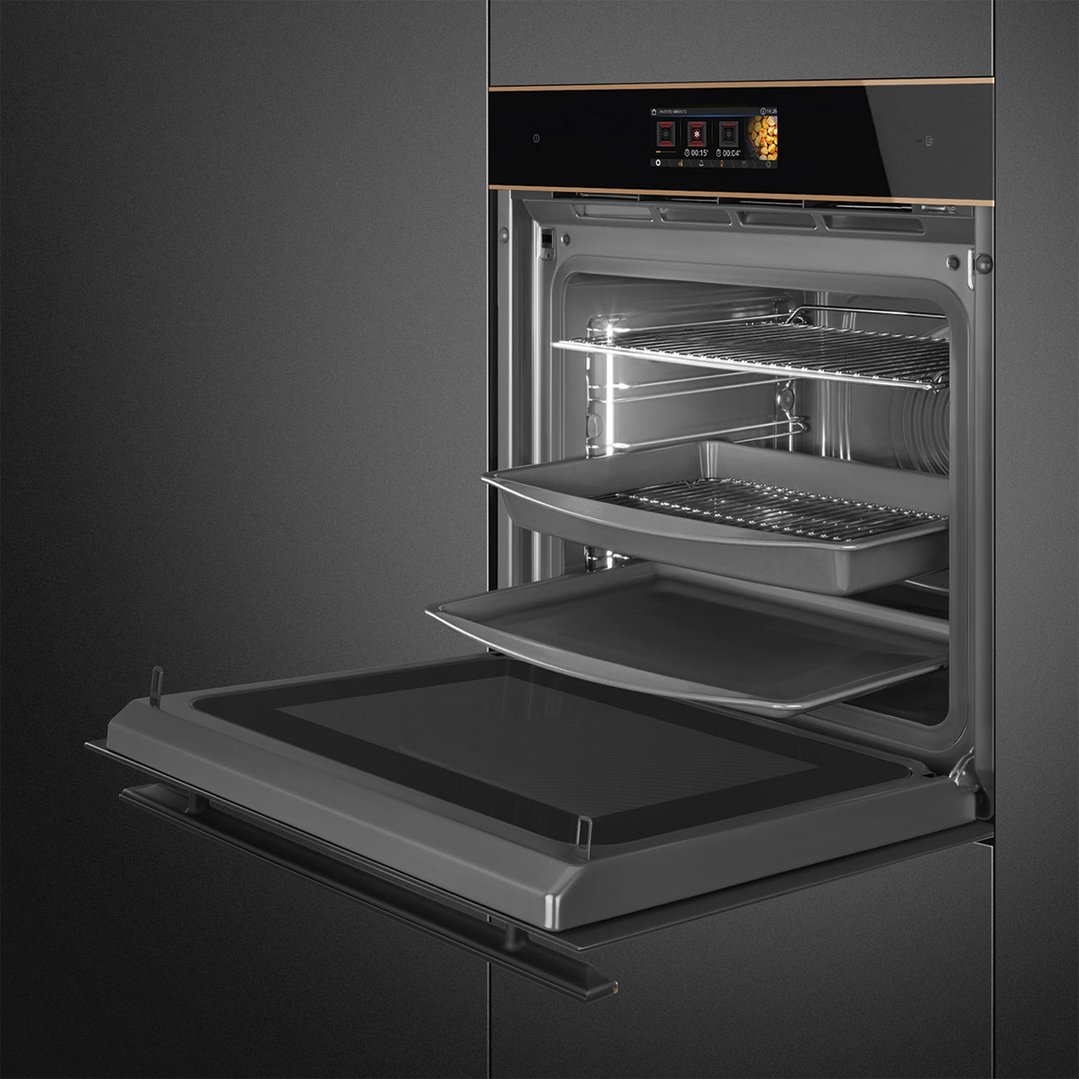 Open black glass oven with copper trim, showing interior racks and trays