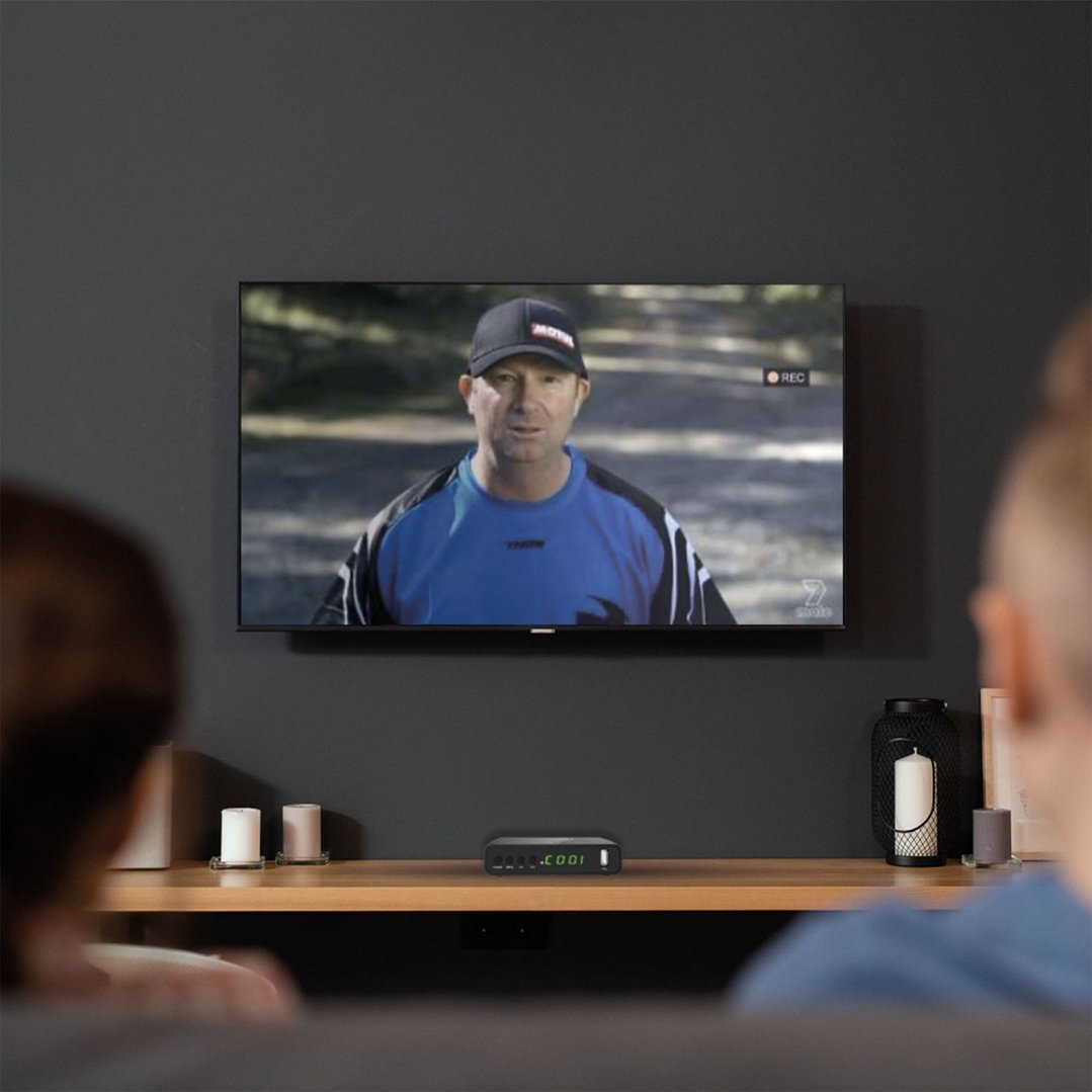Digital Set Top Box on a wooden shelf below a TV showing a man