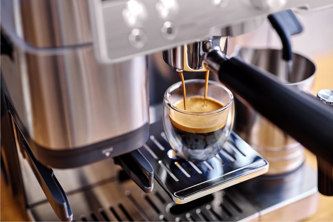 Espresso machine brewing coffee into a clear glass cup on a drip tray
