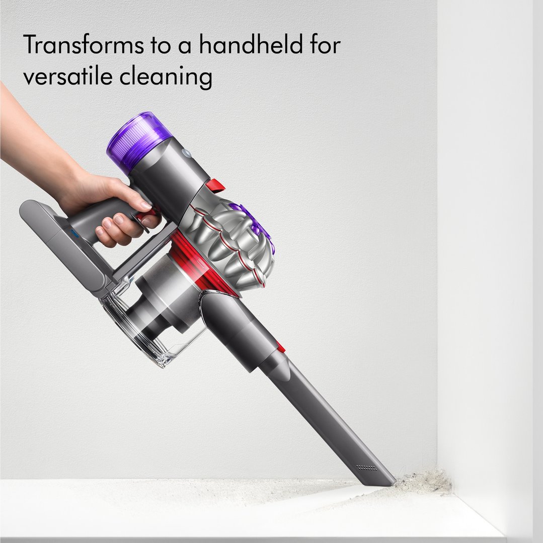 Hand holding a Dyson V8 Advanced Vacuum cleaning a dusty corner
