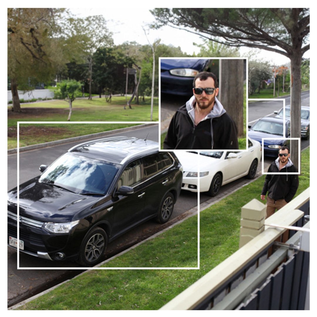 A man in sunglasses and a hoodie walking past parked cars on a street