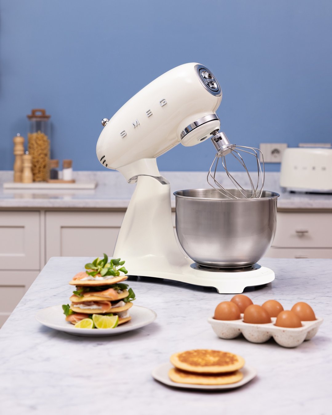 Cream stand mixer on a marble countertop with food ingredients