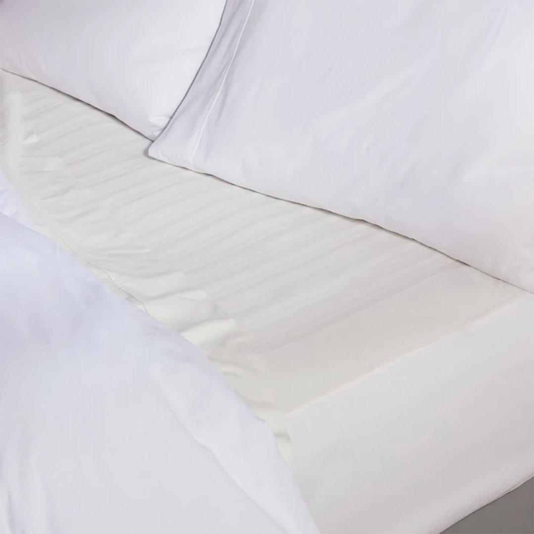 Close up of a white electric blanket with subtle stripes on a bed