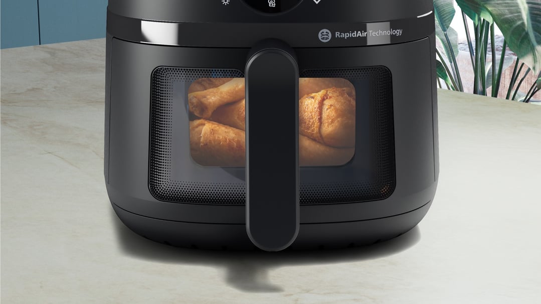 Black airfryer with chicken drumsticks visible through the window on a kitchen counter