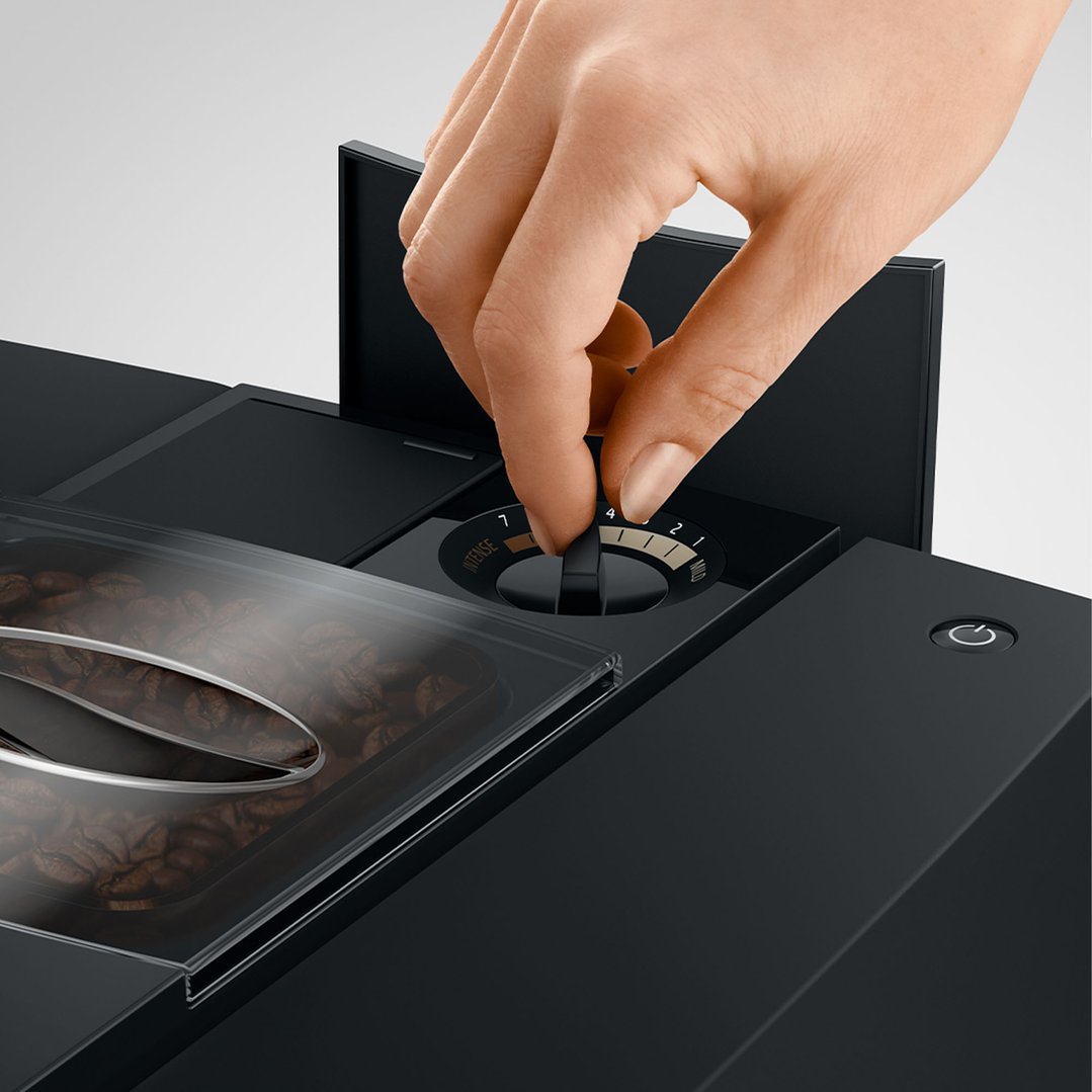 Hand adjusting the intensity dial on a black JURA coffee machine