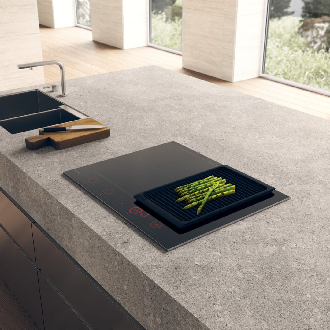 An ASKO induction hob cooktop with a grill pan of asparagus in a modern kitchen