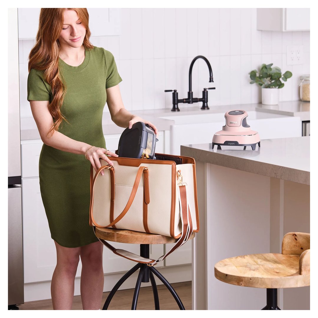 Woman placing a Ninja Crispi air fryer into a large tote bag in a kitchen