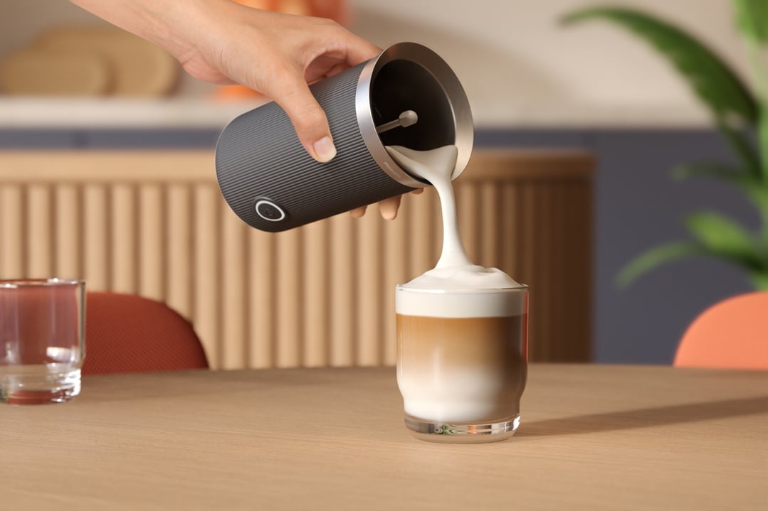 Hand pouring frothed milk from a Philips Baristina Milk Frother into a glass