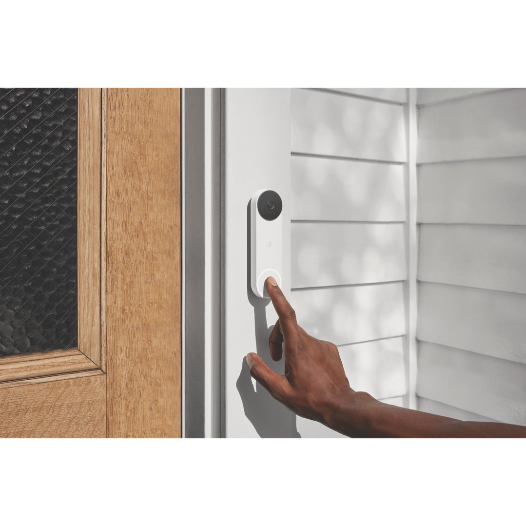 Hand pressing the button on a white Nest Doorbell on a white wall