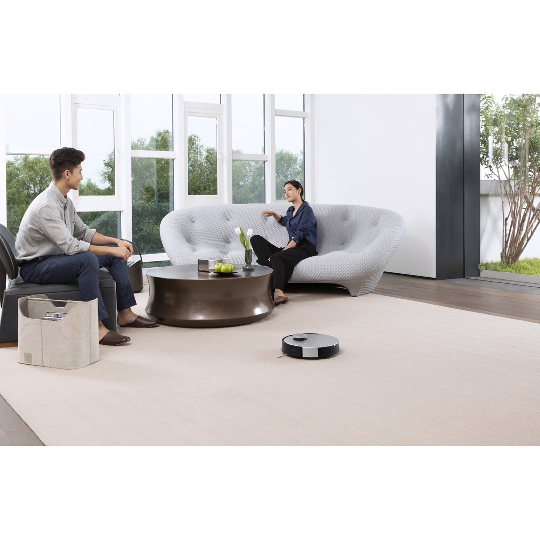 Robotic vacuum cleaning carpet in a living room with two people relaxing