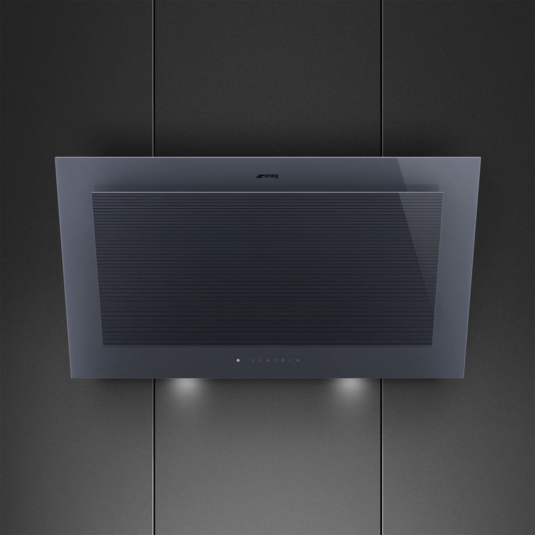 A dark grey vertical rangehood with lights on, mounted on a dark wall