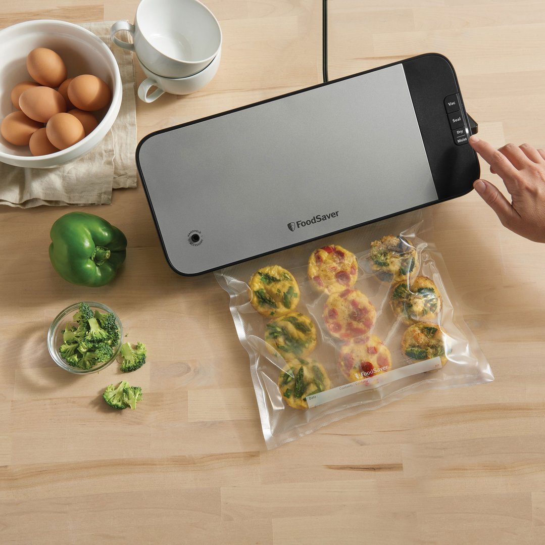 A person's hand operating a vacuum sealer with food in a vacuum bag