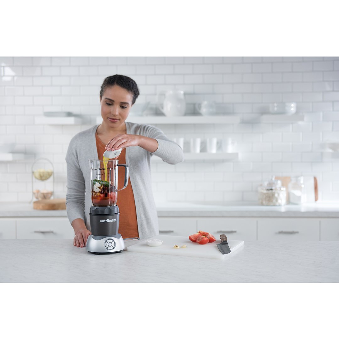 Woman pouring liquid into a blender with ingredients on a kitchen counter