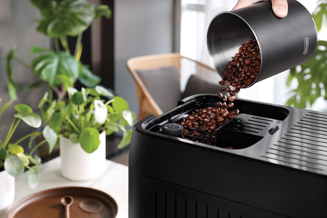Hand pouring coffee beans from a container into a Magnifica Plus Fully Automatic Coffee Machine