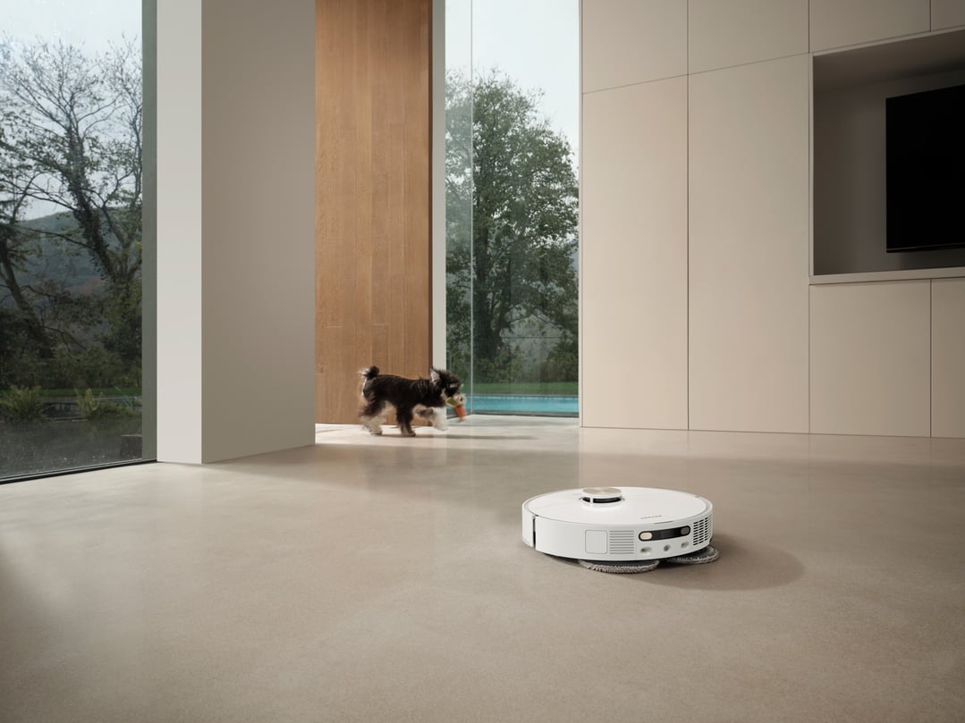 White robot vacuum and mop cleaning a floor in a modern room with a dog