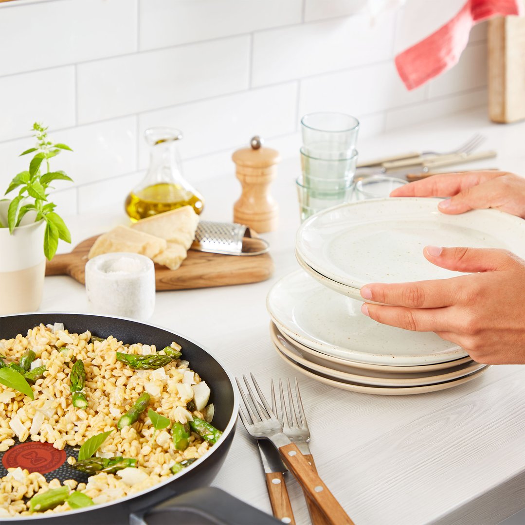 Hands holding plates next to a frypan with food on a kitchen counter