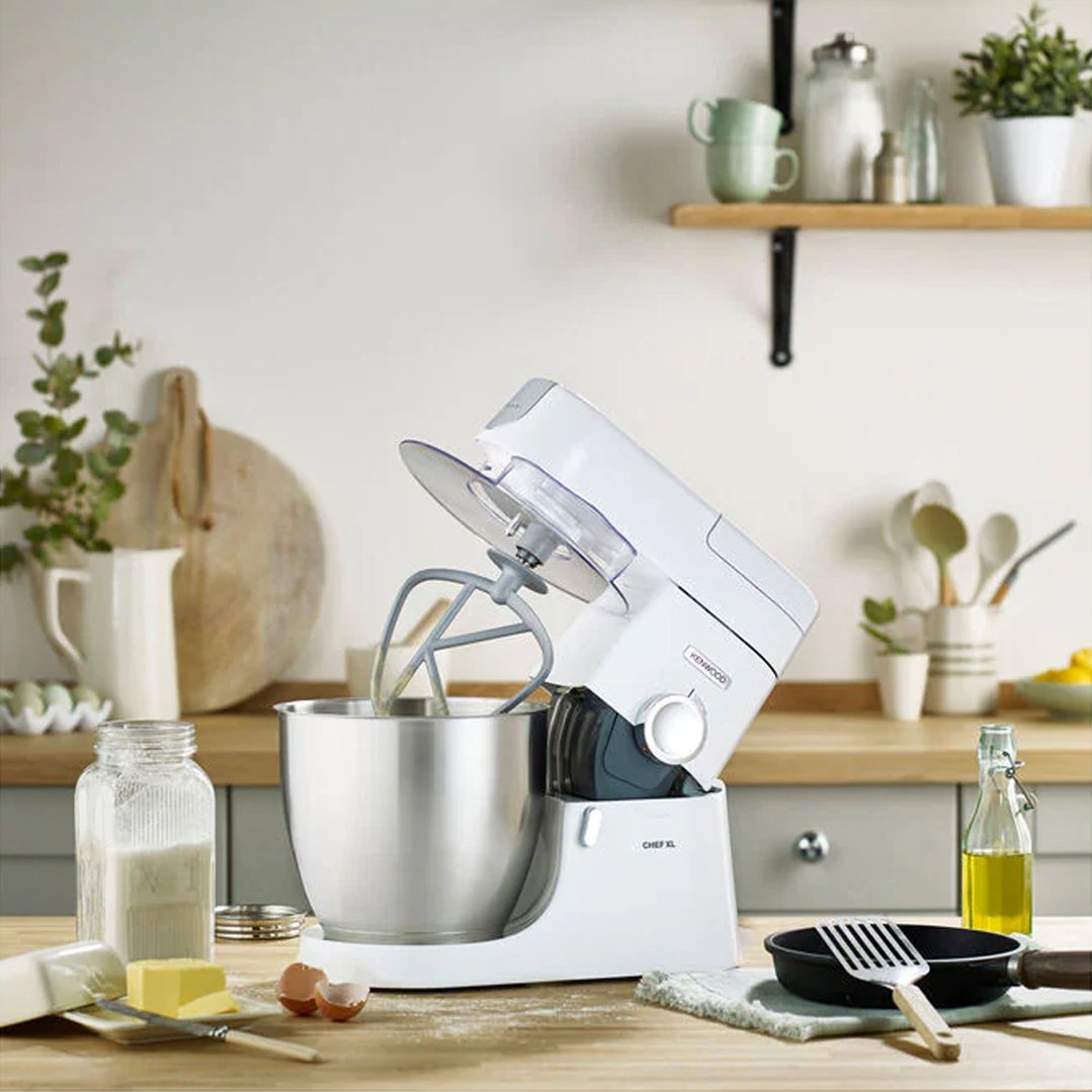 White Kenwood Chef XL Stand Mixer on a wooden kitchen counter with baking ingredients