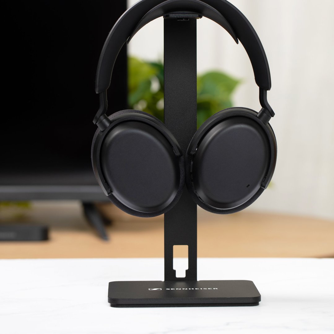 Black Sennheiser TV headphones on a stand in a room with a TV and plant