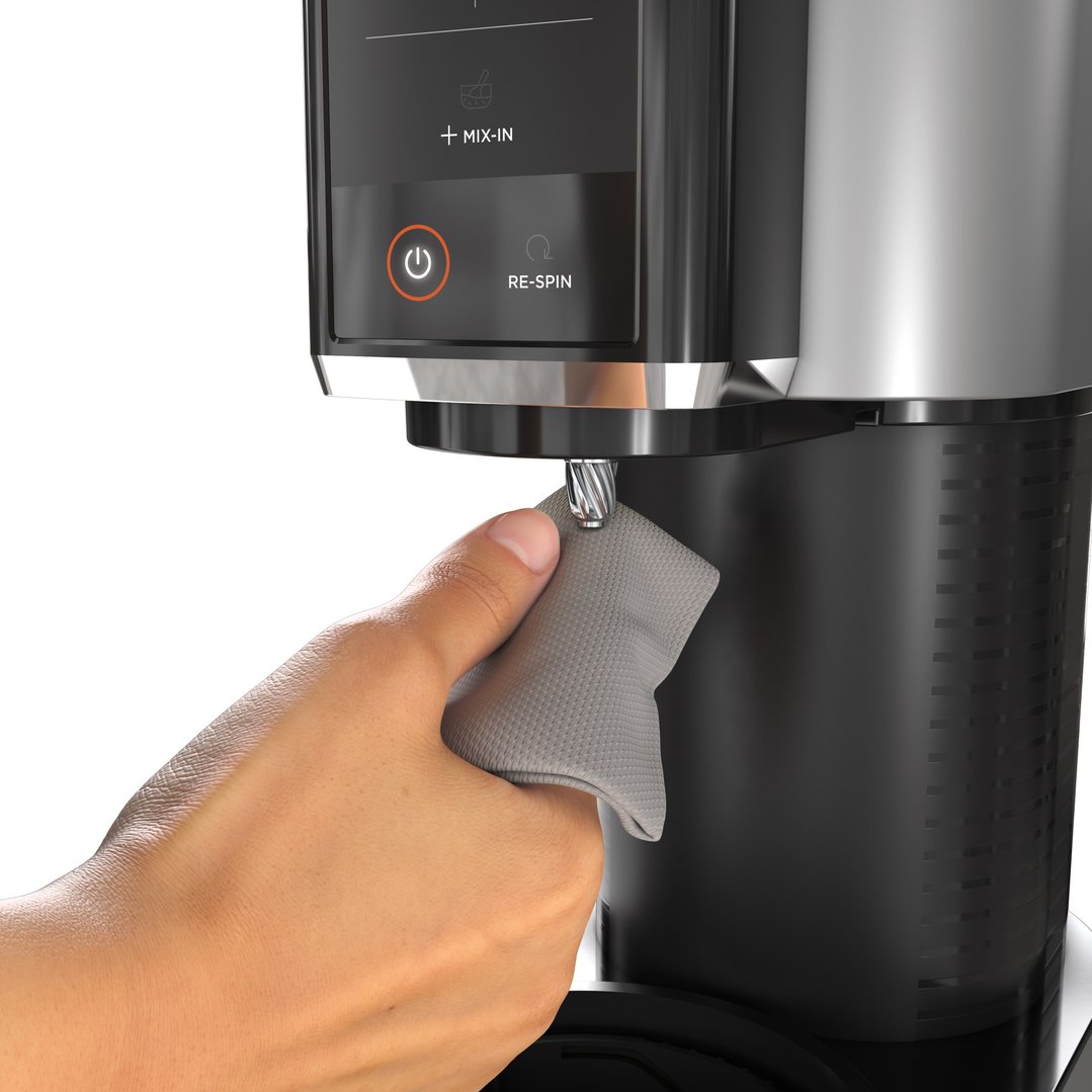 A hand wiping the blade of a Ninja CREAMi Ice Cream Maker with a cloth