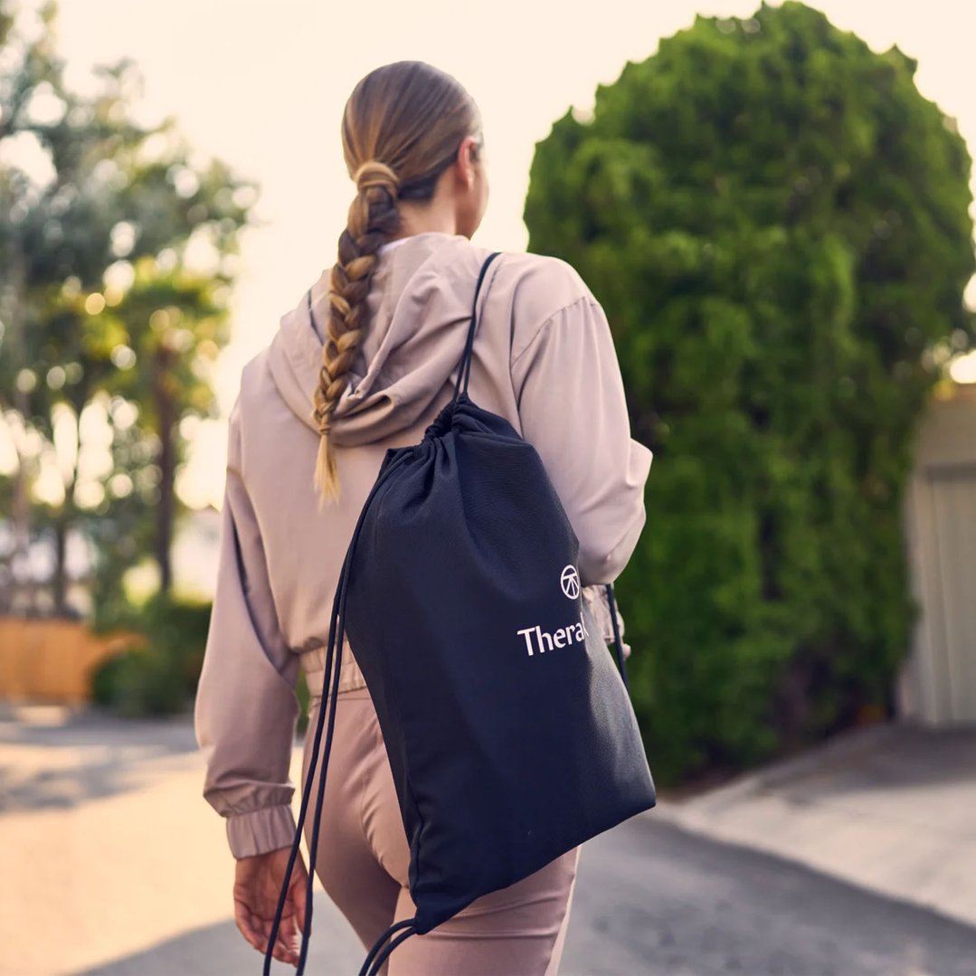 Woman with braided hair walking away, carrying a black drawstring bag