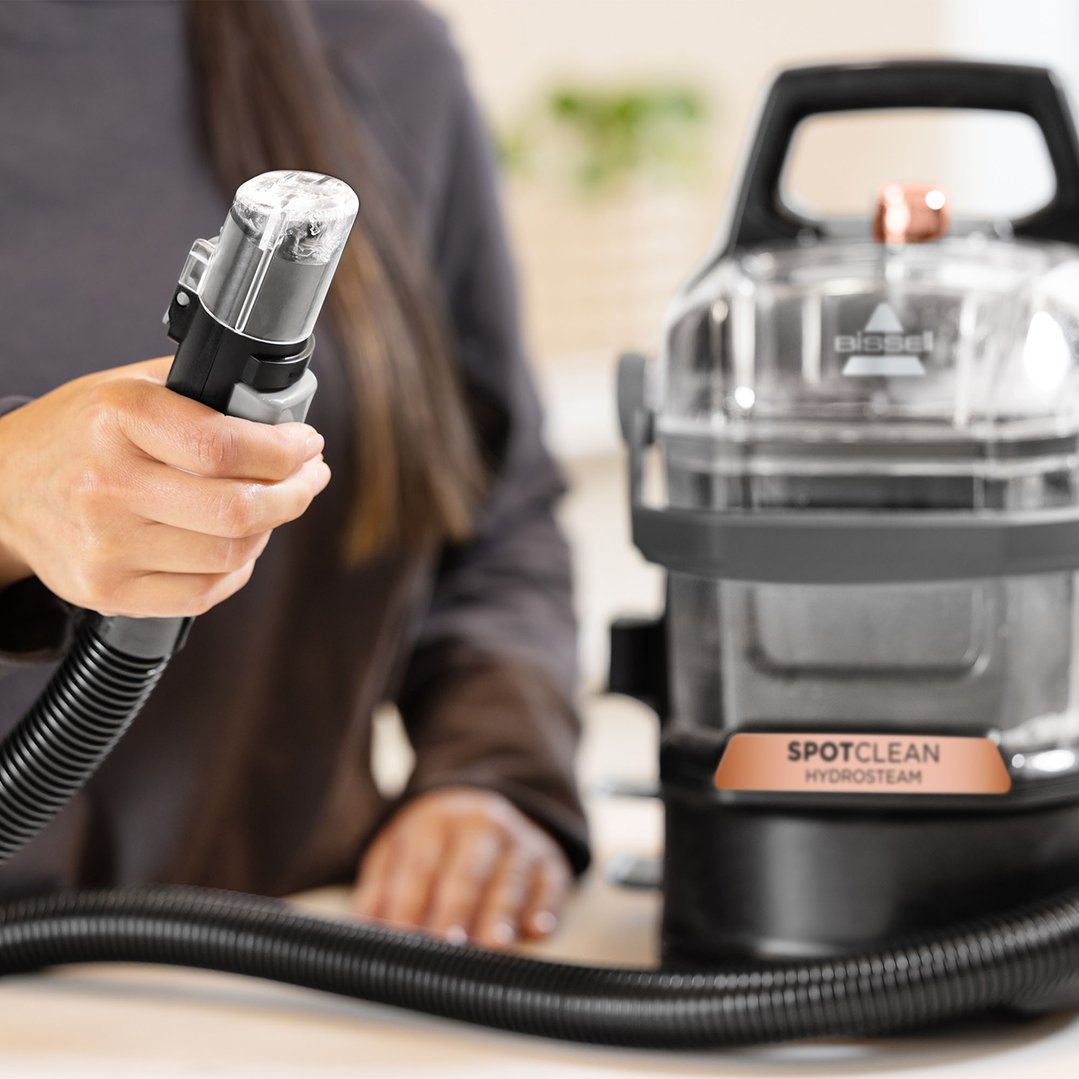 Person holding the hose attachment of a BISSELL SpotClean HydroSteam vacuum cleaner