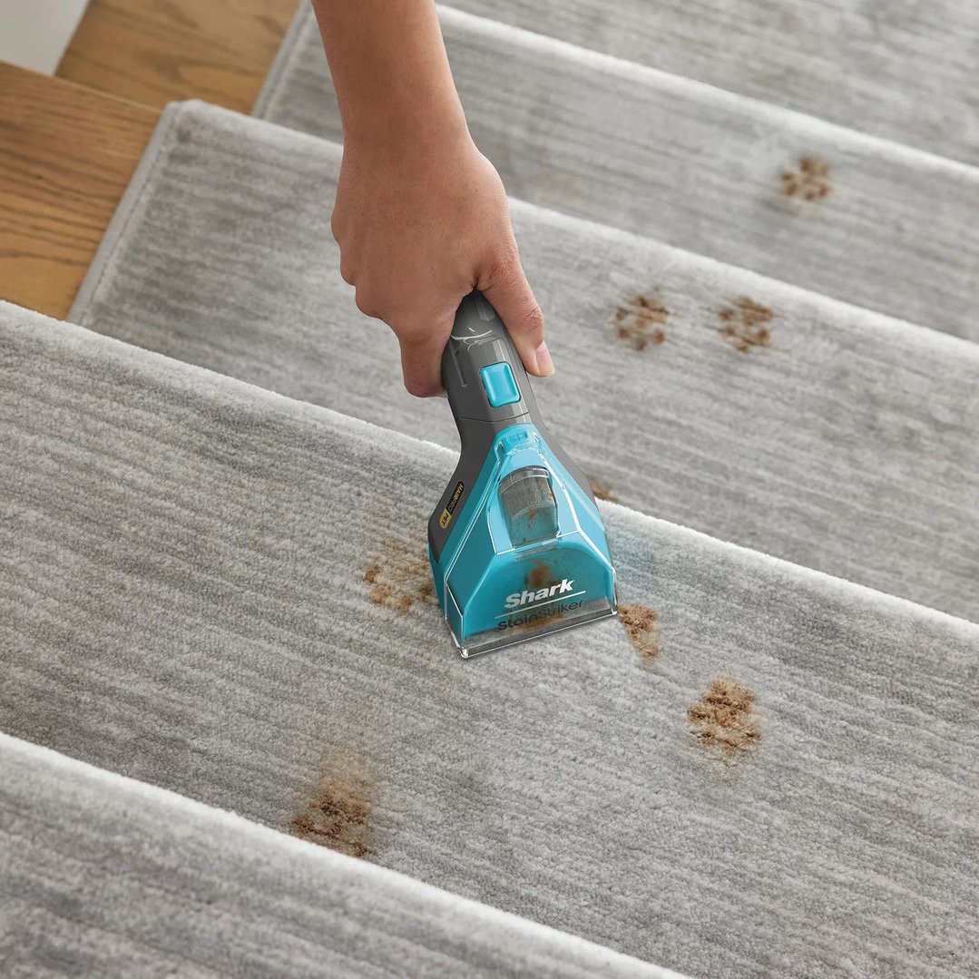 Hand using a Shark StainStriker vacuum cleaner on pet paw prints on carpeted stairs