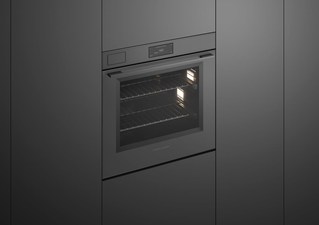 Built-in grey glass oven with interior lights on in a dark kitchen