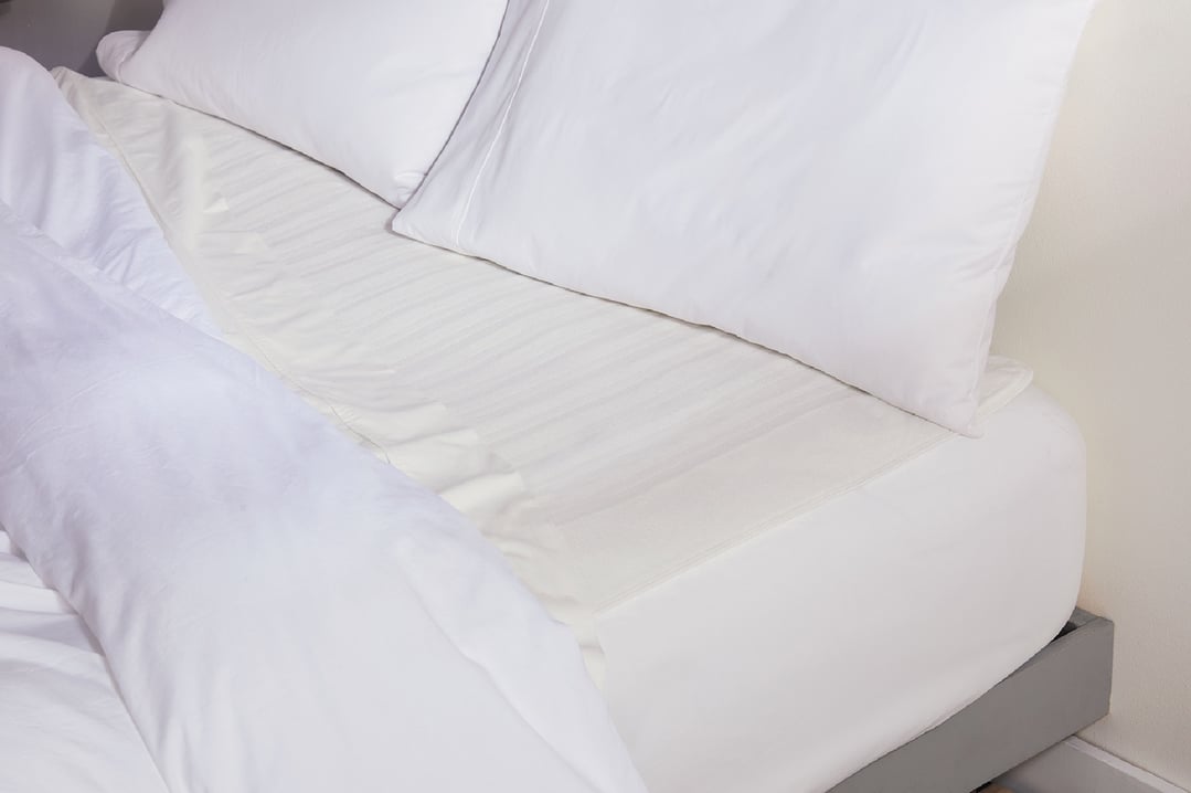 White electric blanket on a bed with white pillows and duvet