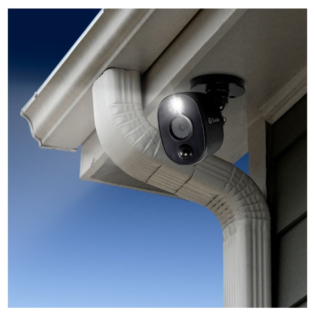 Black security camera mounted under a white eave, with a white downspout