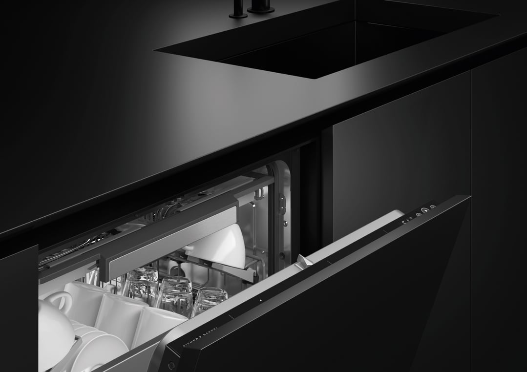 Integrated dishwasher with the door ajar, showing dishes inside a dark kitchen