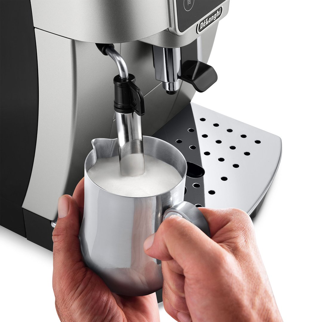 Hands holding a milk jug under the steam wand of a coffee machine