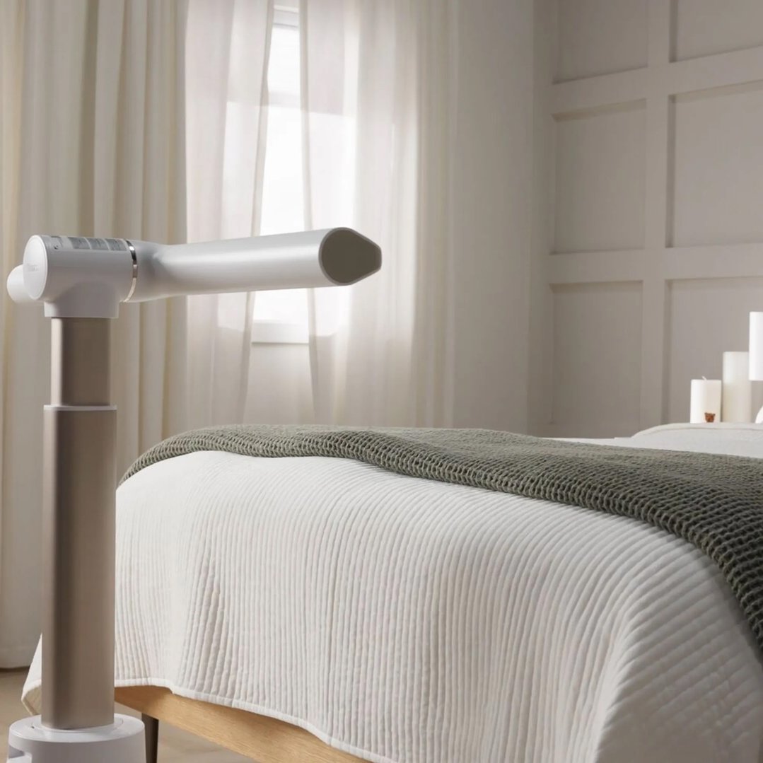 White fan on a stand in a bedroom with a bed and white curtains