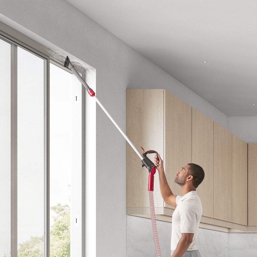 Man using a Dyson vacuum cleaner to clean dust from a window frame