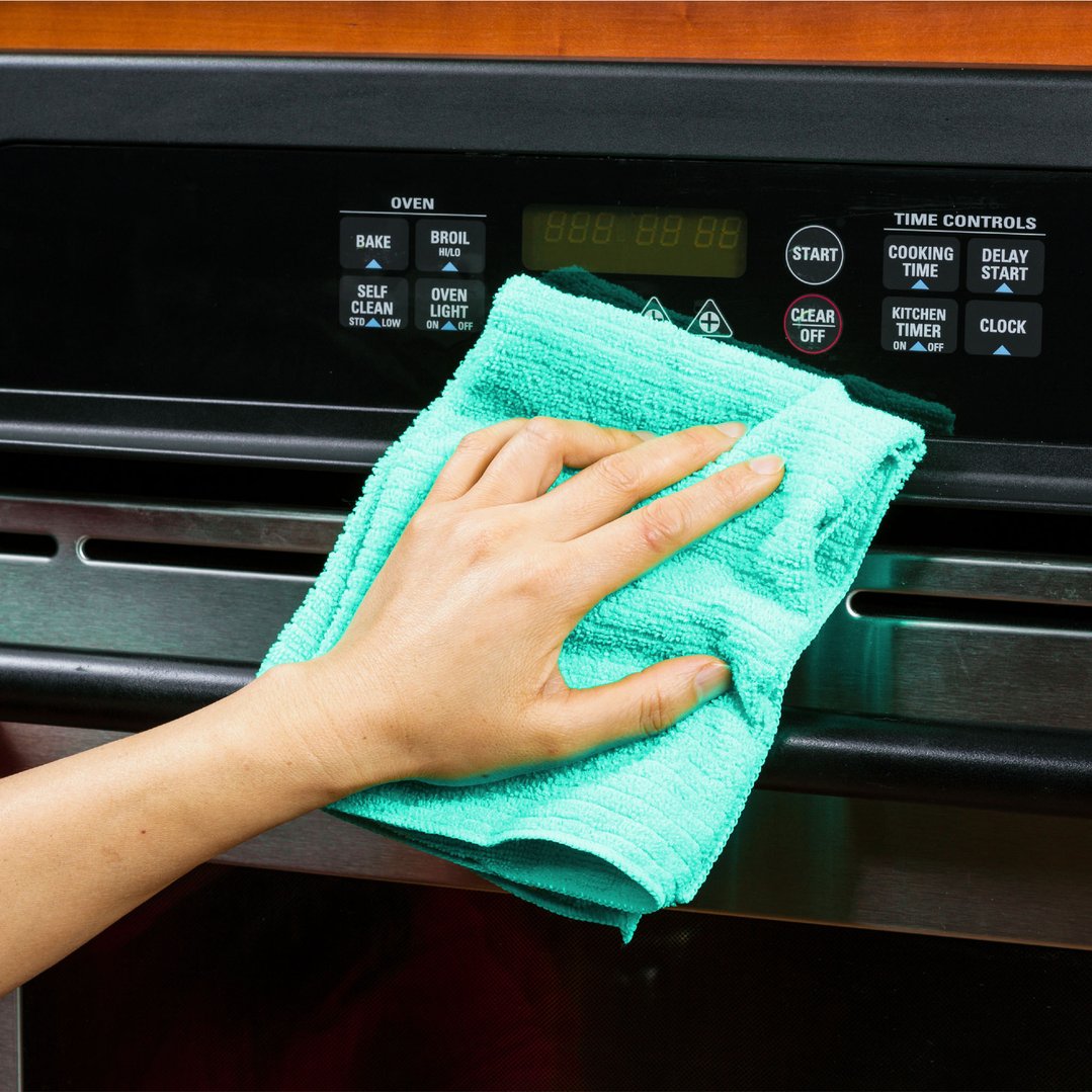 Hand wiping down an oven control panel with a teal cleaning cloth