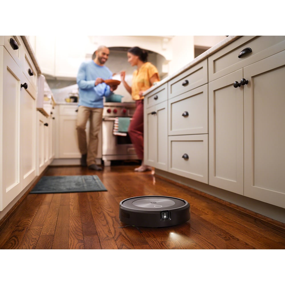 Roomba j7+ Robot Vacuum cleaning a wooden floor in a kitchen with two people