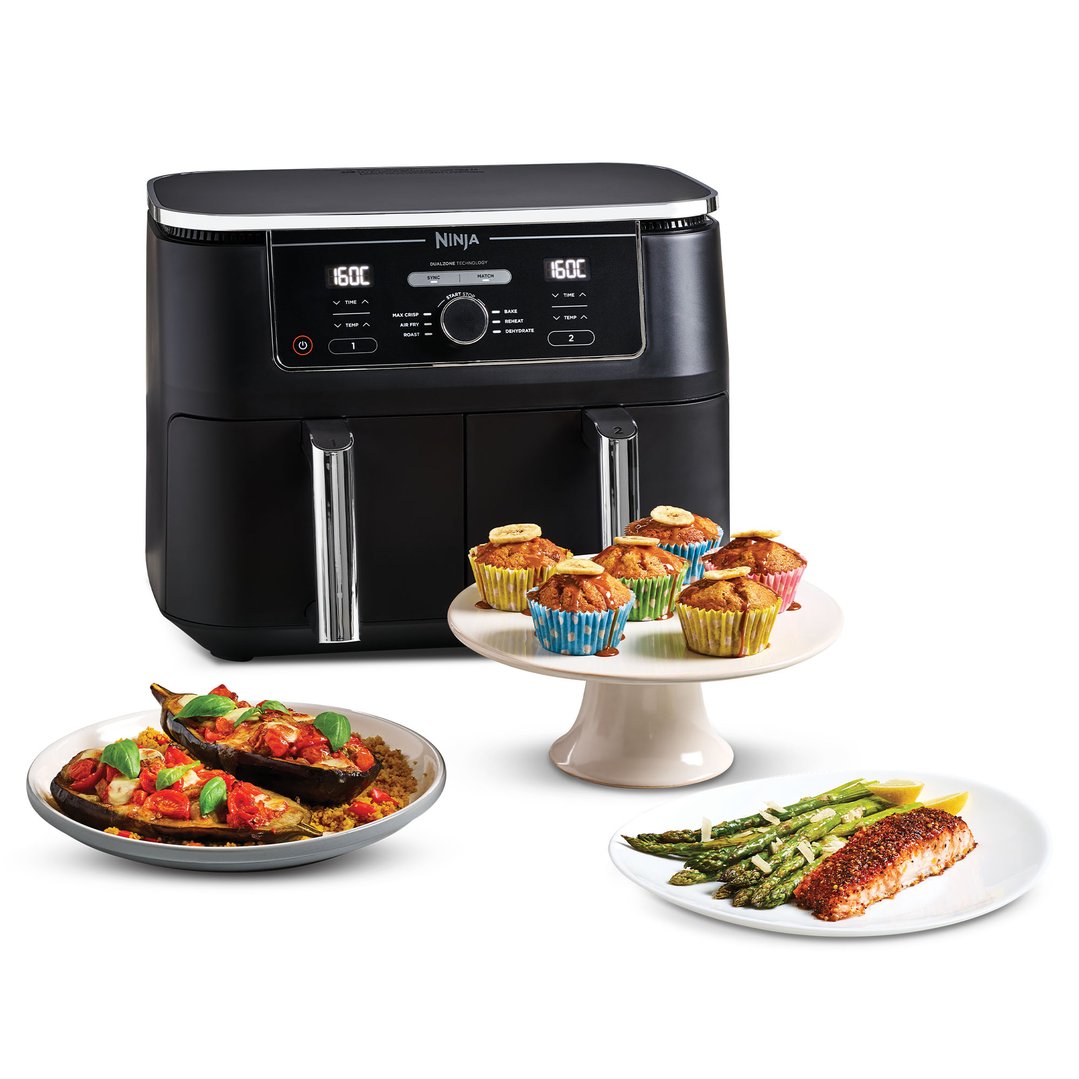 Ninja Foodi MAX Dual Zone Air Fryer with cooked food on plates and a cake stand