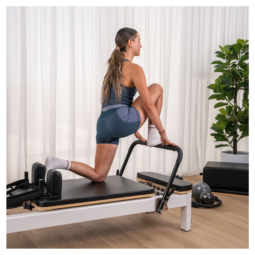 Woman exercising on a Pilates Reformer in a bright room with sheer curtains
