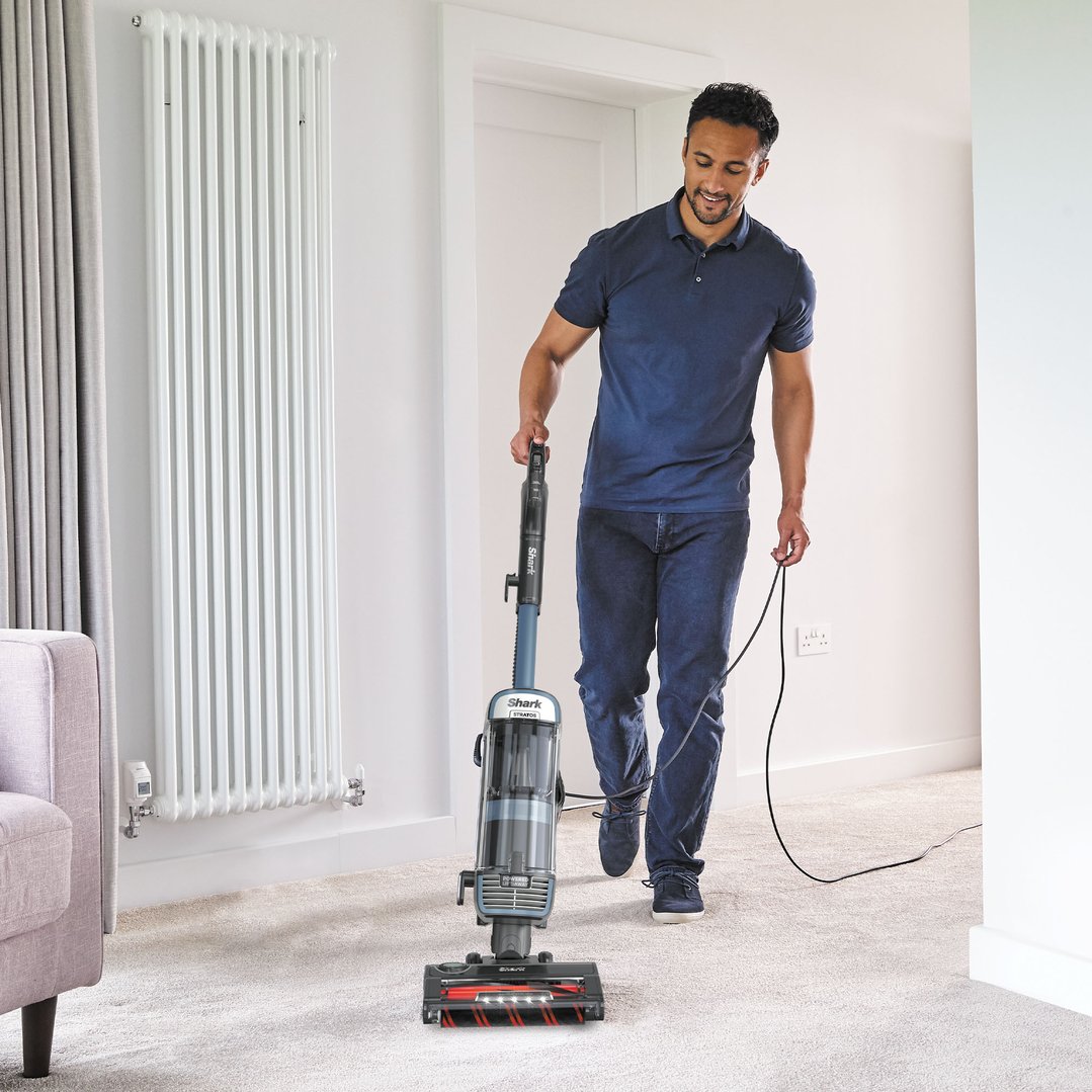 Man vacuuming a light-colored carpet with a Shark Stratos vacuum cleaner