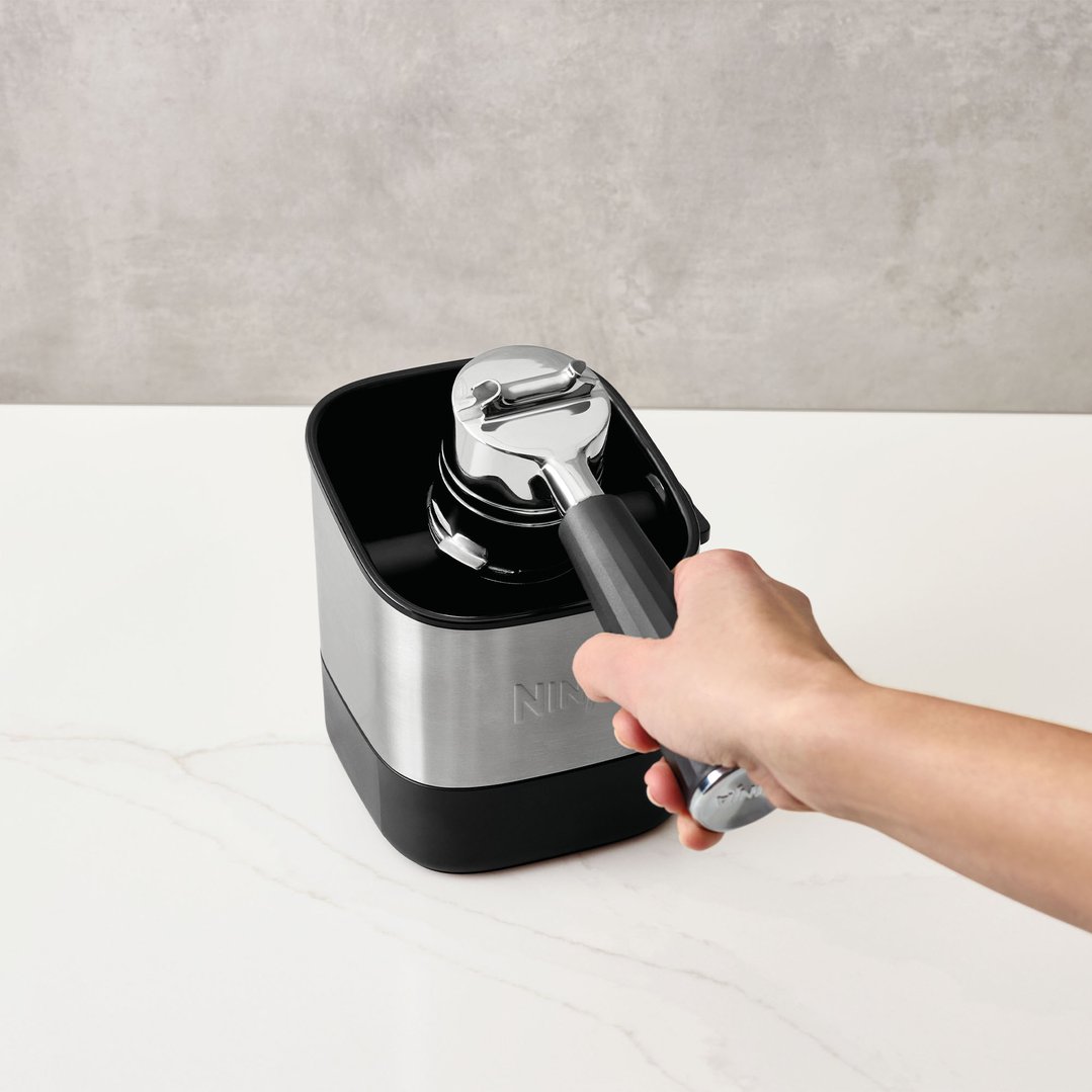 Hand holding a portafilter over a Ninja Luxe Café Knock Box